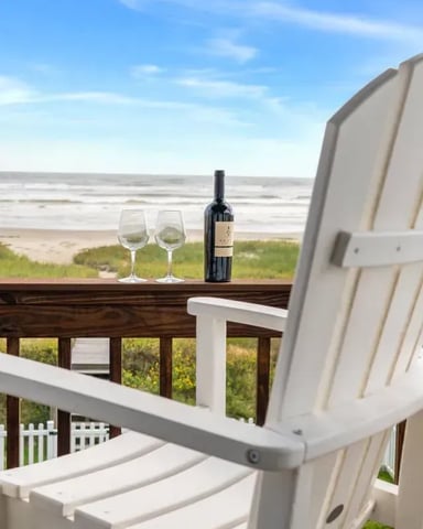 White Adirondack chair on beach deck with wine bottle and glasses overlooking ocean