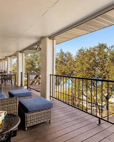 Covered deck with wicker seating, water view, trees, and metal railing overlooking pool and lake