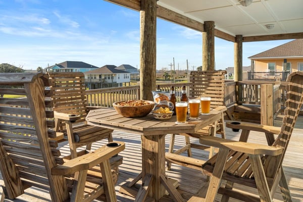 Covered wooden deck with dining table, Adirondack chairs, beers and snacks, overlooking coastal neighborhood and water