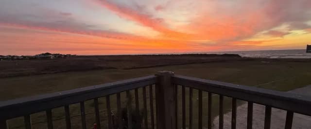Wooden deck railing overlooking coastal marsh at sunset with orange and pink sky